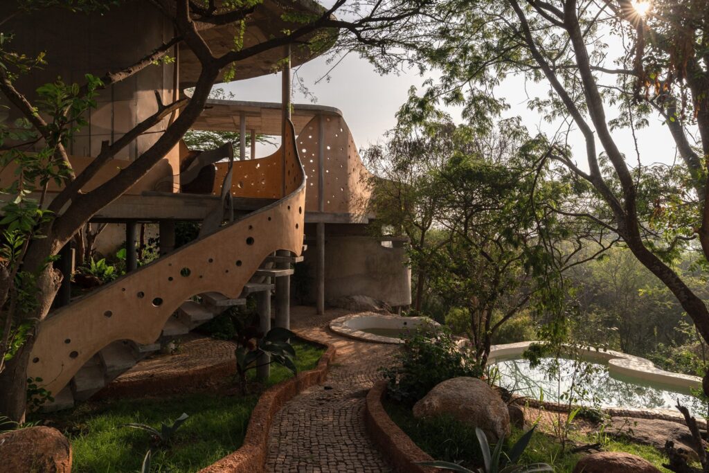 Индийская студия Prithvi Architects завершила строительство Winterfell — глинобитного дома, построенного вокруг существующих деревьев и скальных образований в деревне Шулагири в штате Тамил Наду.